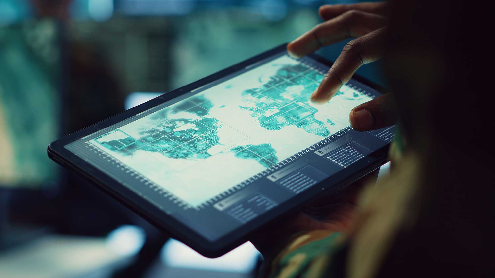 A person holds a tablet displaying a digital world map with highlighted locations. The dimly lit background suggests a tech-focused, analytical setting.